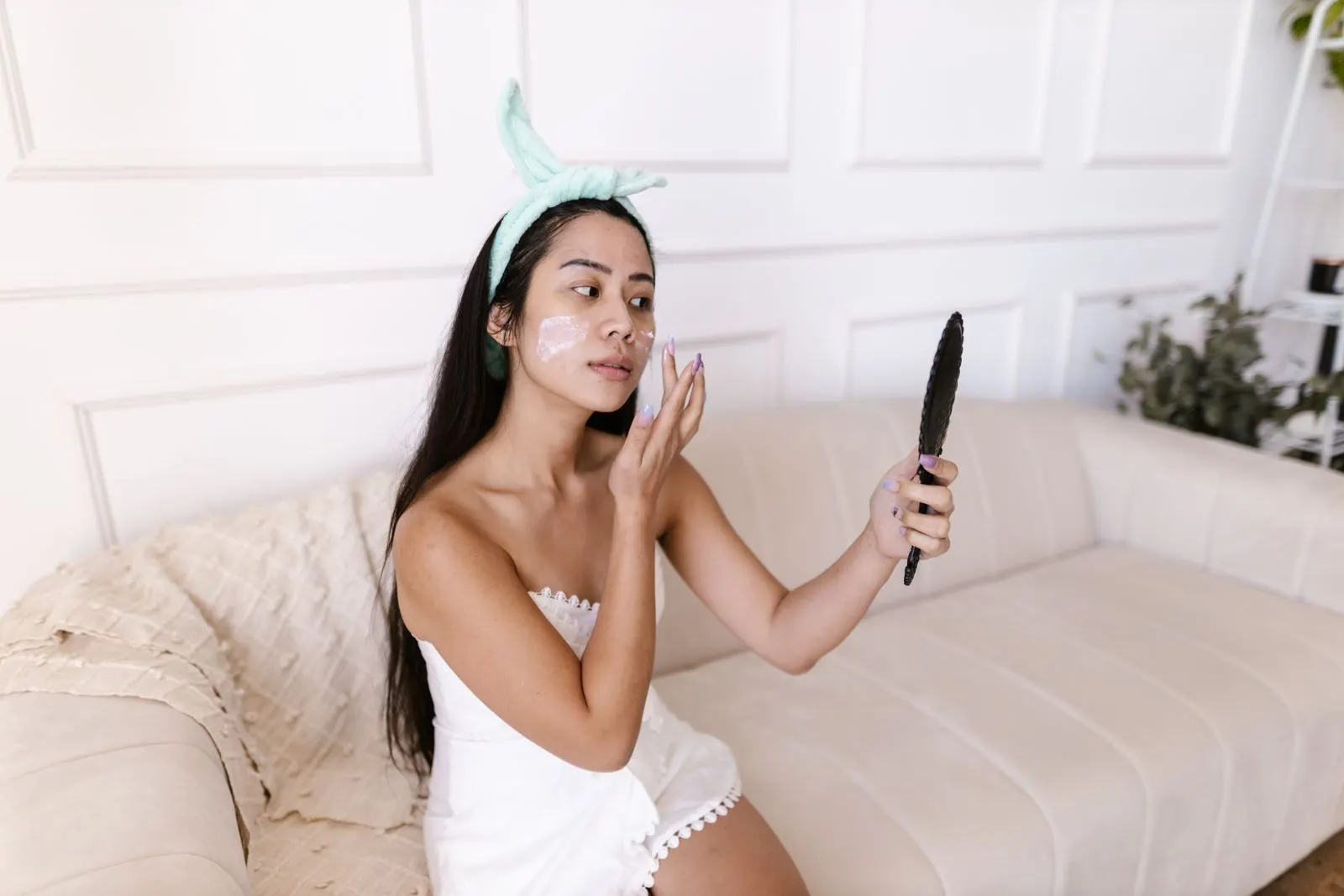 ソファで手鏡を見ながらスキンケアをする女性